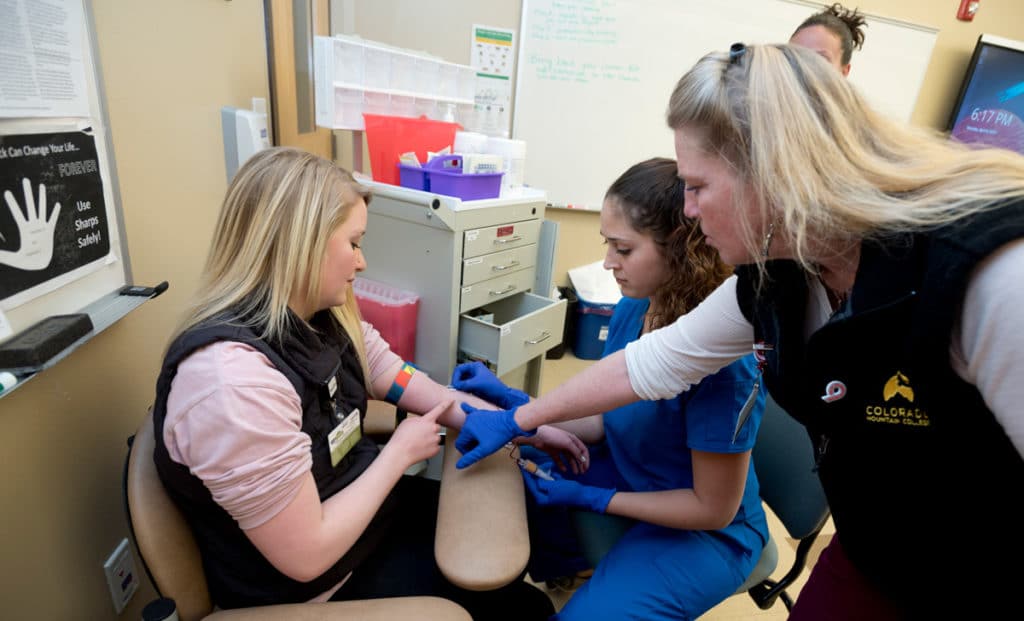 CMC Phlebotomy students performing a blood draw in a lab with a CMC professor.