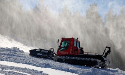 A CMC "snowcat" drives up a slope with snowmaking in the background.