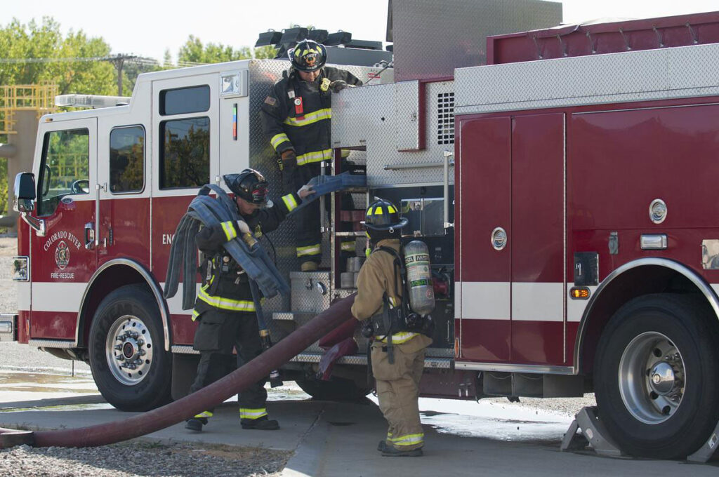 CMC Firefighting students pull hoses from a firetruck at a training session.