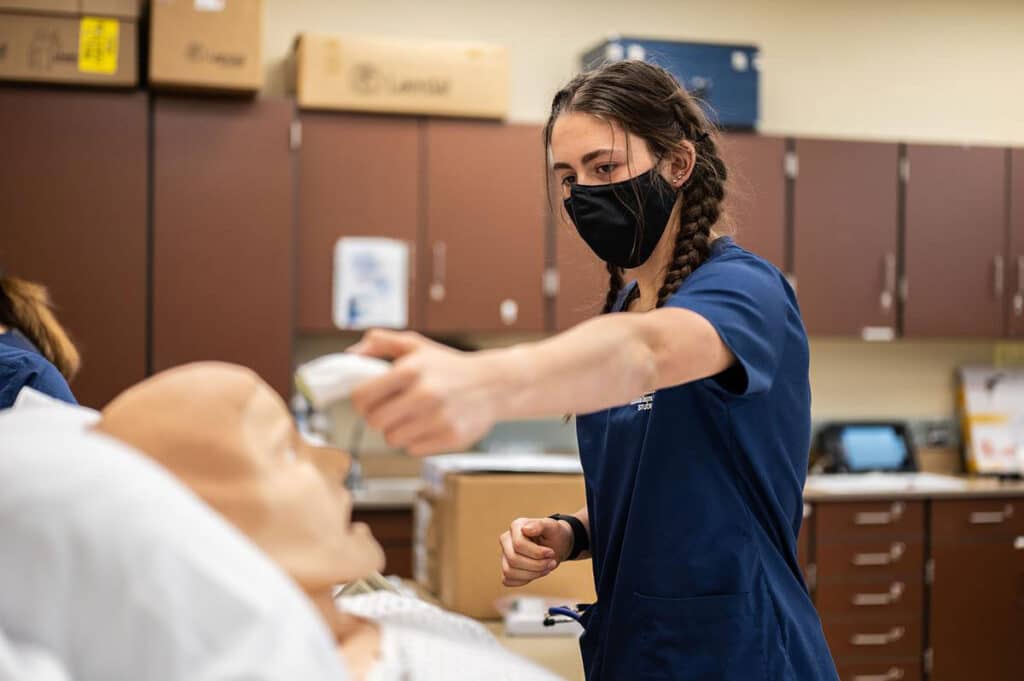 Nursing student checking patient temperature in a practice lab.